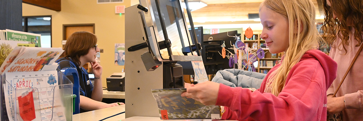 Young girl and mother checking out items at the library's circulation desk