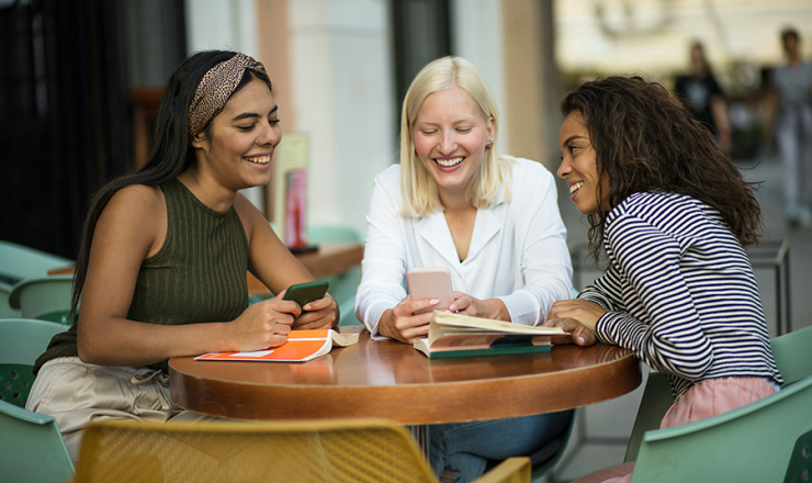 Group of three women sitting at a table with books and smartphones