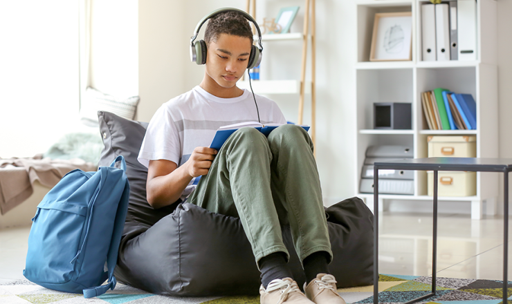 Teen boy sitting on bean bag with an open book and headphones on