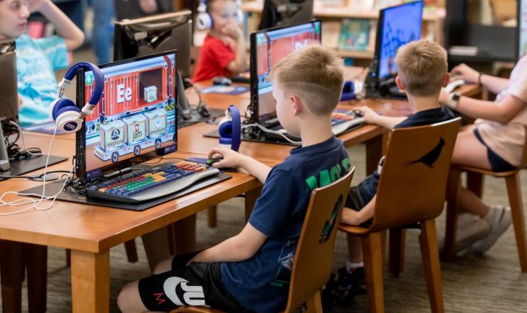 Children sit at educational computer stations in the library playing games